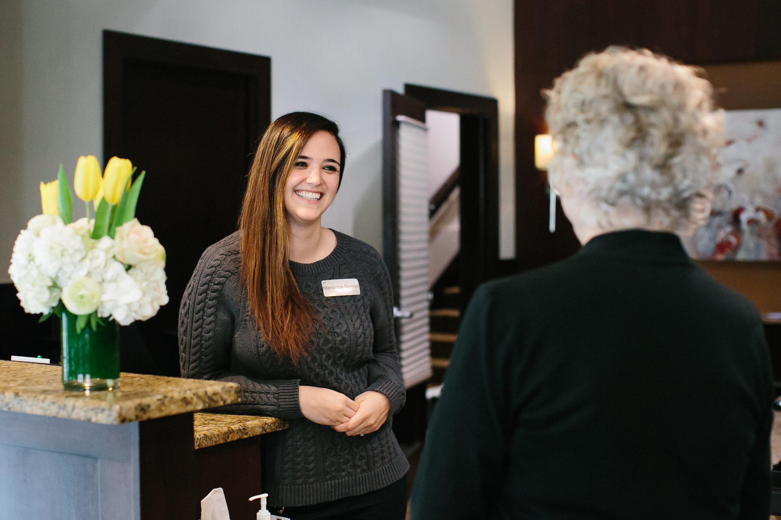 A desk clerk smiles at an older person, who is facing away from the camera