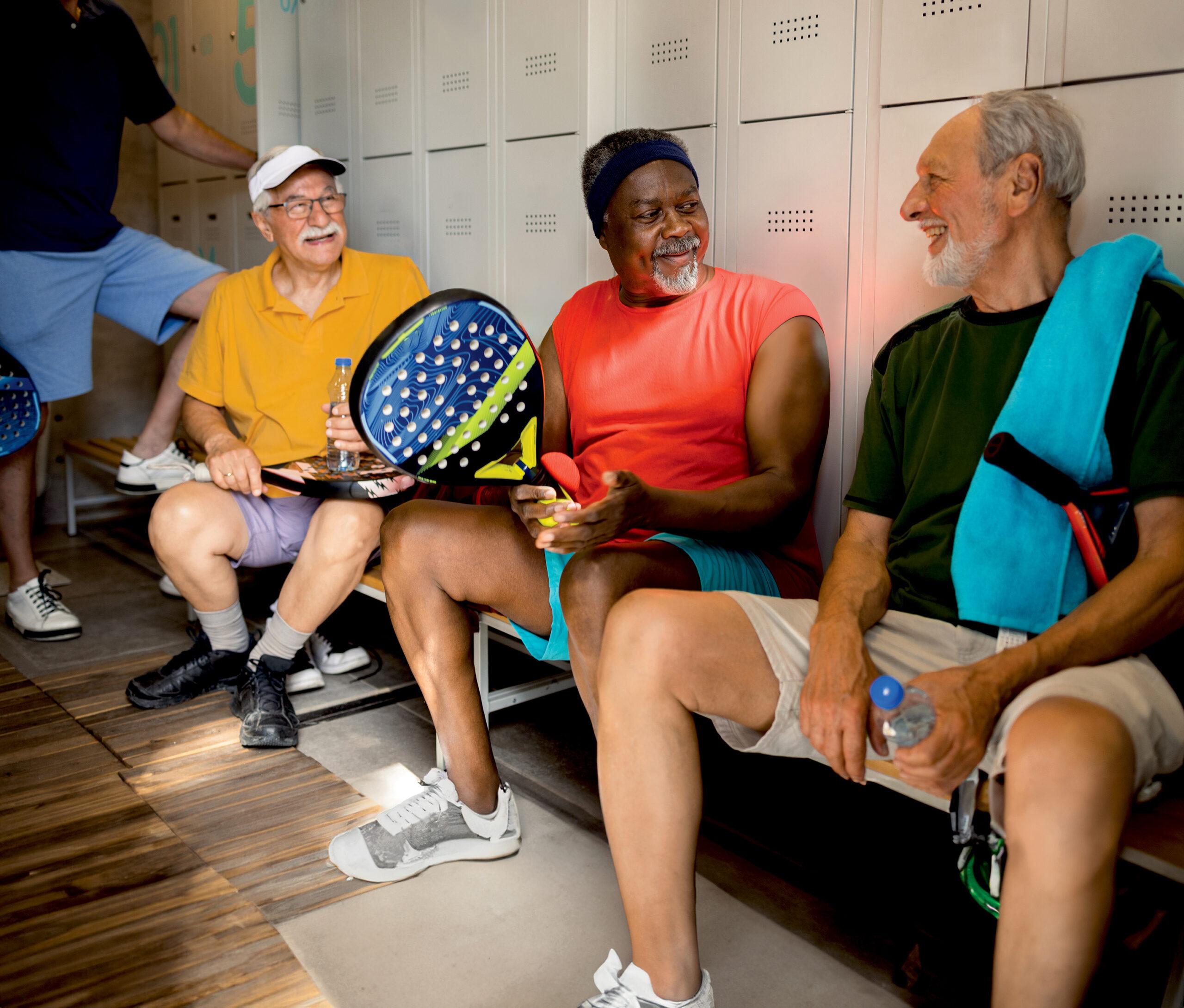 Older friends talk and laugh in the locker room after a game of Paddle Tennis