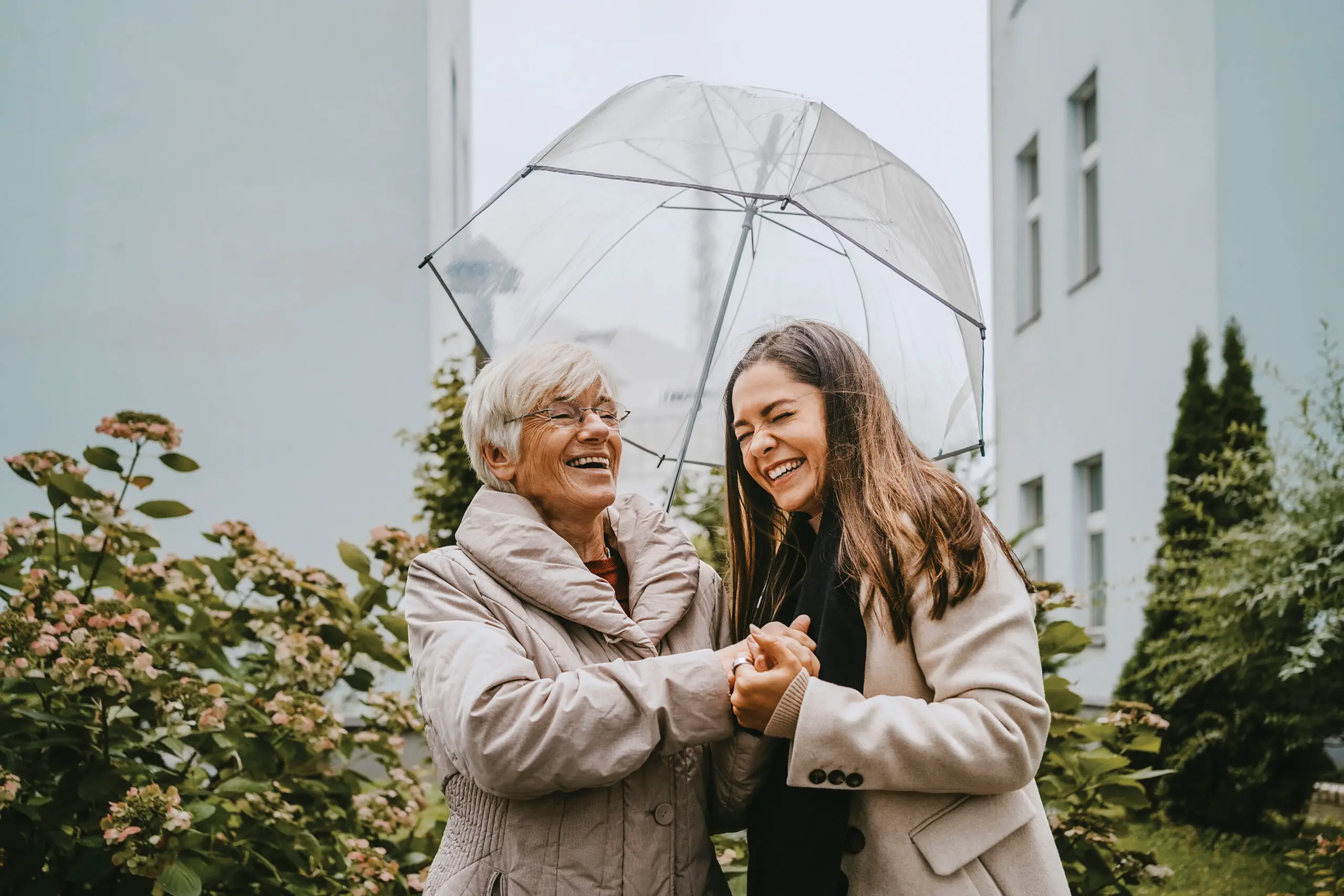 A happy older woman and younger woman walk together holding an umbrella over them