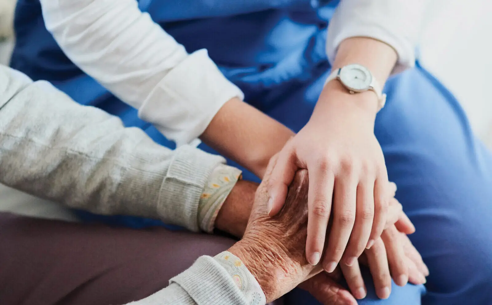 A nurse compassionately holds a patient's hands. Their faces are not in the photo